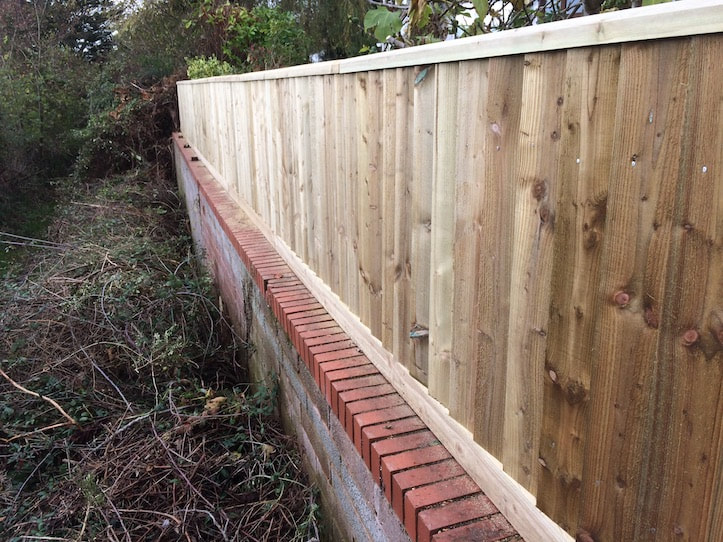 wooden fence built on breeze block and brick capped wall